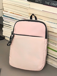 Rosa Nylon-Umhängetasche mit schwarzem Reißverschluss und Tragegriff auf Büchern