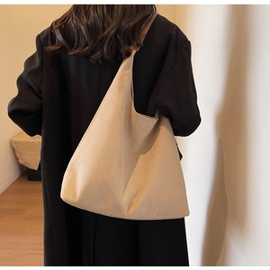 Detail of a large beige shoulder bag with brown leather straps worn by a model