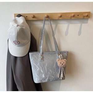 Detail of silver tote bag with crinkled leather texture and plush bear charm decoration