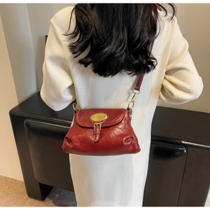 Detail of dark red pleated leather shoulder bag with gold metal plaque on model