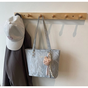 Detail of silver tote bag with crinkled texture, brown plush bear charm and fashion logo