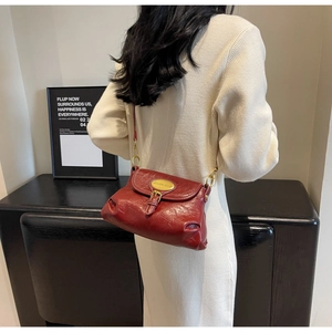Detailed close-up of dark red vintage shoulder bag featuring golden metallic buckle and logo