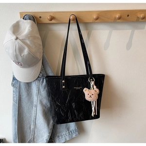 Detail of black pleated faux leather tote bag with a cute bear plush keychain