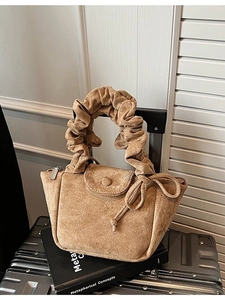 Brown faux suede bucket bag featuring ruffled handle and decorative bow accent