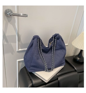 Detail einer dunkelblauen Denim-Einkaufstasche mit silbernen Ketten auf einer Bank