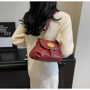 Detail of wine red glossy pleated shoulder bag with gold logo and vintage flap closure