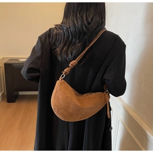 Close-up of brown suede half-moon bag with knot detail worn by a model in a black coat