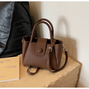 Detail of dark brown pebble leather handbag featuring a round clasp and adjustable strap