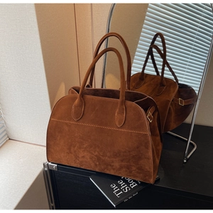 Détail d'un sac cabas en daim marron avec fines anses et boucles dorées latérales