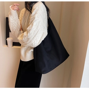 Minimalist black large capacity tote bag worn on shoulder in a cozy indoor setting