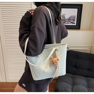 Detailed side view of light green textured tote bag with cute brown plush bear charm
