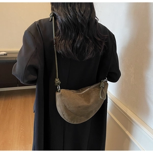 Olive green suede half-moon crossbody bag featuring stylish knotted strap detail on black blazer