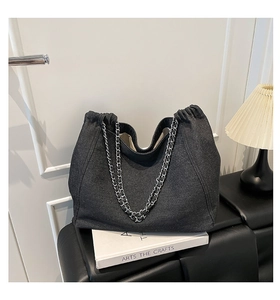 Detail der dunkelgrauen Denim-Tote-Bag mit silberner Kette auf einer Bank