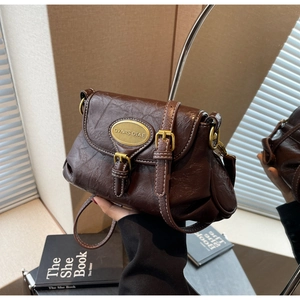 Detail of dark brown vintage crossbody bag with white stitching and metal logo plaque