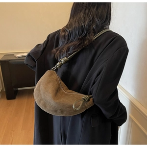 Detail showing deep moss green suede crescent bag with elegant knotted shoulder strap design