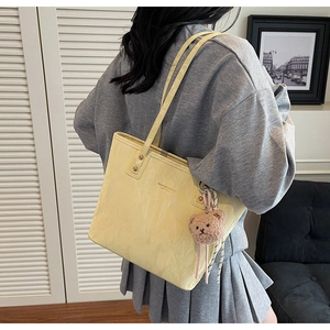 Detail of light yellow tote bag with pleated texture and cute brown teddy bear charm