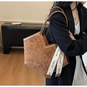 Close-up of brown suede tote bag featuring minimalist leather logo and text webbing