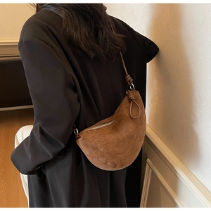 Detail of a brown suede crescent bag featuring a decorative knot strap and silver zipper