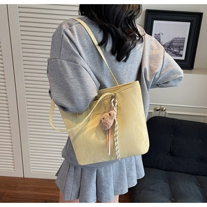 Detail of light yellow pleated tote bag featuring a cute plush bear pendant accessory