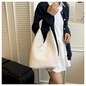 Dettaglio di una borsa hobo color crema in morbida pelle pieghettata sulla spalla di una donna