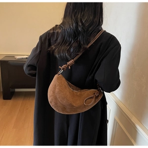 Detail of a brown suede crescent bag featuring a textured finish and stylish knot shoulder strap