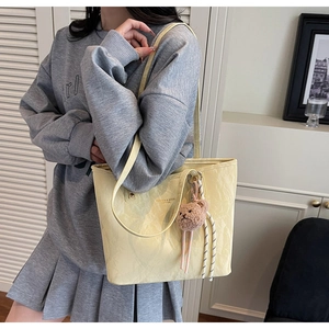 Detail of light yellow leather tote bag with pleated texture and cute bear charm