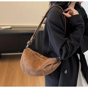 Brown suede crossbody bag with knot detail worn by a model in a minimal setting