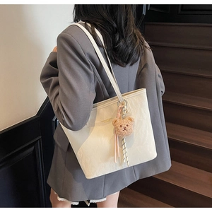 Detail of a creamy white textured tote bag with a brown plush bear charm accessory