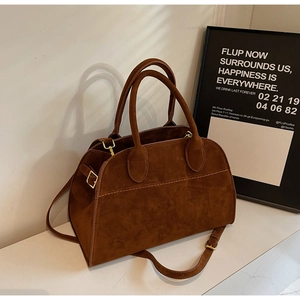 Détail du sac Boston en daim marron avec boucles dorées et doubles poignées de main