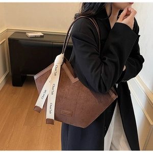 Detail of dark brown matte tote bag featuring decorative white ribbon and square logo