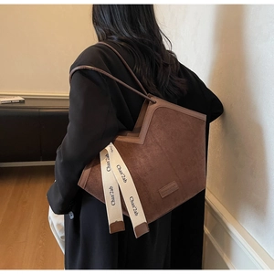 Detail of vintage brown suede tote bag with decorative lettered ribbon and long shoulder straps