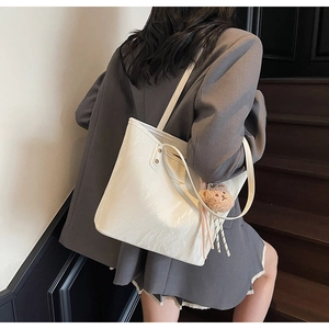 Detail of white glossy leather tote bag featuring minimal text and a brown plush bear charm