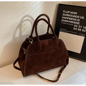 Sac Boston en daim marron avec boucles dorées et bandoulière sur plan en marbre