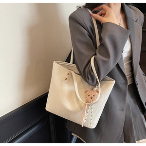 Detail of white leather tote bag featuring a cute brown plush bear charm and gold lettering