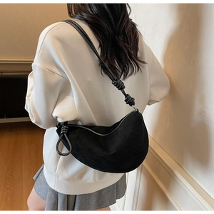 Detail of black suede crescent bag with knot strap shown on model for stylish drape