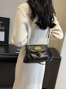 Elegant black pleated leather crossbody bag with gold buckle on a model's white dress