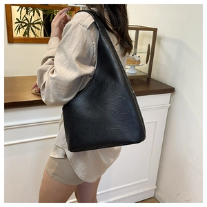 Vista laterale della borsa hobo nera in pelle plissettata indossata da una modella al caffè