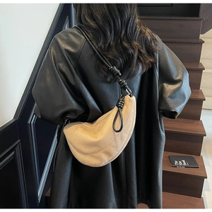 Detail of beige suede half-moon bag featuring knotted shoulder strap and sleek design