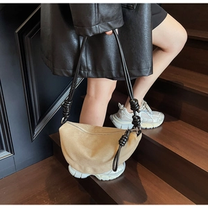 Detail of khaki suede crescent bag with black leather braided knot strap on wooden stairs