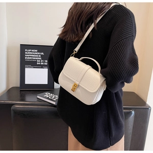 Close-up of white lychee leather texture and gold twist lock on women's handbag