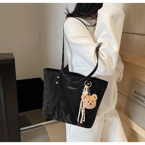 Close-up of black pleated tote bag with golden lettering and a cute plush bear charm
