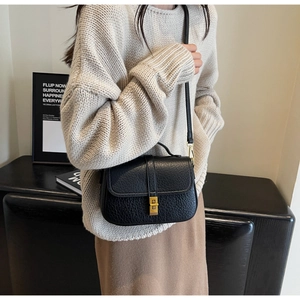 Side view of woman wearing black grain leather saddle bag with vintage gold clasp