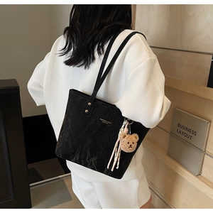 Detail of black wrinkled leather tote bag with plush bear charm on slender straps