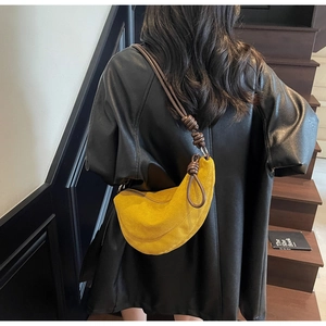 Detail of yellow suede crescent bag with dark brown knotted leather strap on black coat
