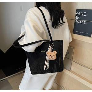 Detailed view of black tote bag with wrinkled leather texture and plush bear pendant