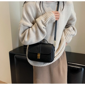 Detail of black litchi grain leather square bag with gold metal buckle on a beige sweater