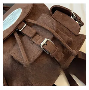 Détail du sac à dos en daim marron foncé montrant le logo argenté et les boucles