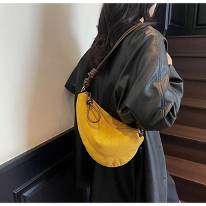 Detail view of yellow crescent suede bag featuring brown knotted leather strap and metal zip