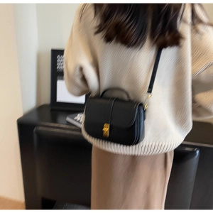 Detail showing a black crossbody square bag with a gold metal clasp worn by a model