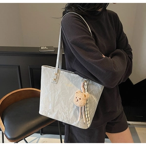 Detail shot of light grey tote bag with pleated texture and plush bear accessory